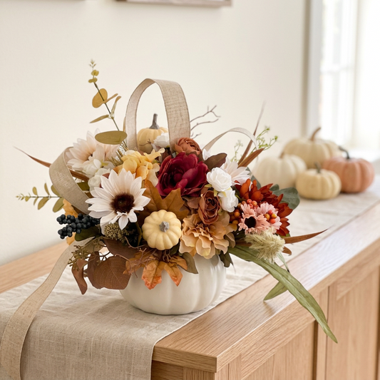 A ceramic container with a variety of artificial fall flowers including pumpkins, gourds, and autumn foliage.