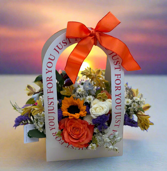 Floral arrangement in a decorative paper bag with an orange ribbon 