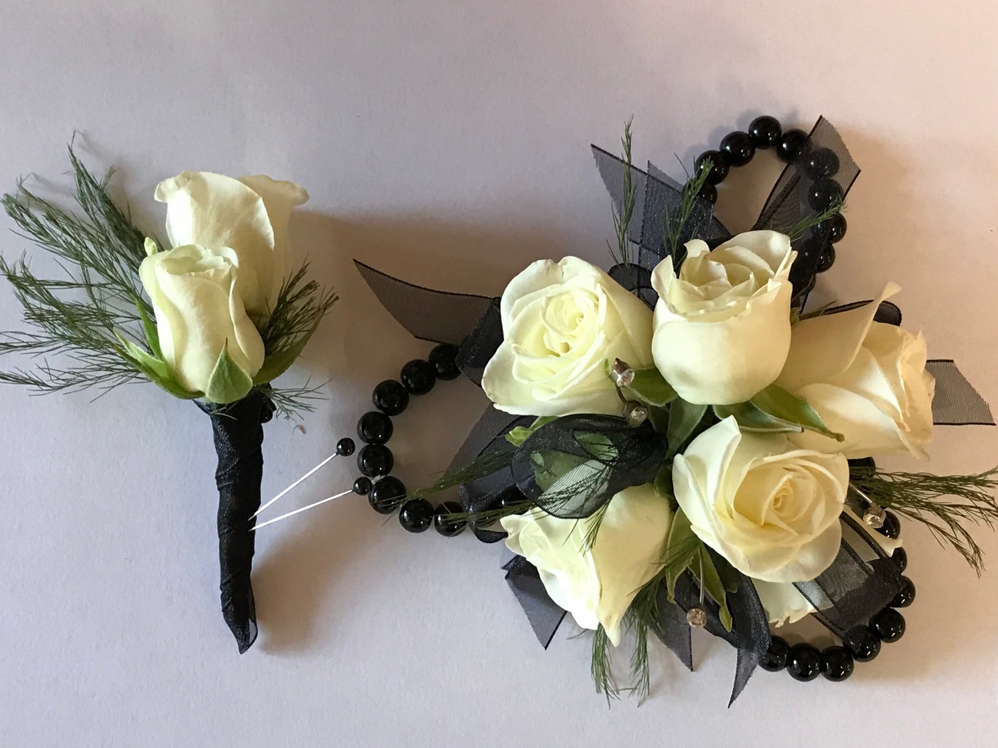 Wrist Corsages with white roses, black beads, and green leaves on a light gray background.