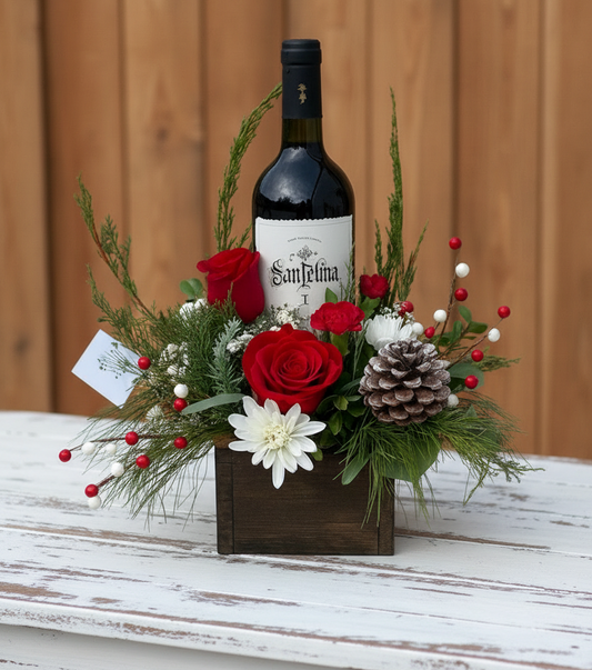 Wine bottle in a decorative floral arrangement with red roses and greenery on a neutral background